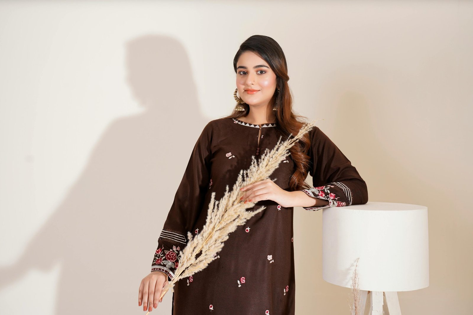 Portrait of a young woman in an embroidered brown dress holding dried flowers, styled elegantly indoors.
